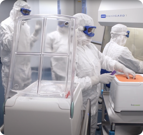 Lab technicians working in full clean-room conditions, with head-to-foot coveralls, eye and face masks.